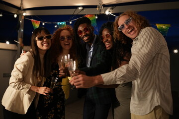 Multiethnic friends toasting at rooftop party with colorful sunglasses