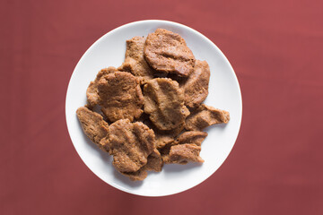 Overhead view of kuli-kuli in a white bowl, top view of nigerian groundnut cakes in a bowl, fresh homemade nigerian kulikuli in a ceramic bowl