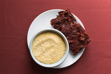 Overhead view of Nigerian kilishi and yellow garri on a white plate, top view of garri and nigerian spicy beef jerky, flatlay of cassava granuls and dried beef suya
