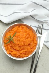 Tasty mashed sweet potato with rosemary in bowl served on grey textured table, flat lay