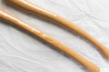 Overhead view of iloka candy on parchment paper, top view of cooked condensed milk candy shaped into a log, Nigerian iloka candy on a white background, process of making caramel hard candy