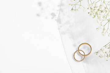 Golden wedding rings, veil and flowers on white background, top view. Space for text