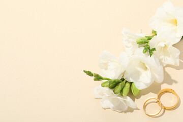 Golden wedding rings and flowers on beige background, above view. Space for text