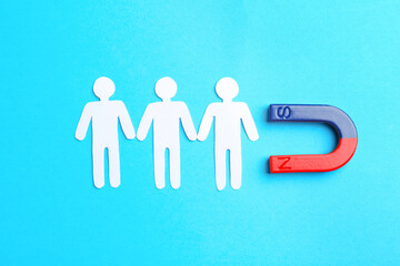 Magnet attracting paper cutouts of humans on light blue background, flat lay