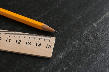 Wooden ruler and pencil on black table, closeup. Space for text
