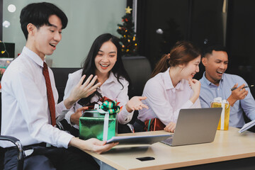 full length view of a group of business team wearing red Santa hat and exchange gift box together in the office for Christmas.