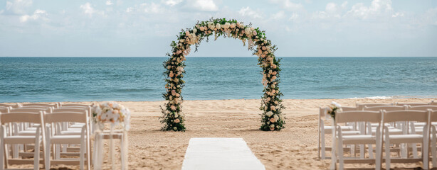 picturesque beach wedding setup featuring floral arch and white chairs, creating romantic atmosphere by ocean. serene backdrop enhances beauty of occasion