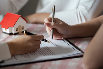 Signing Real Estate Contract with Model House on Table - Close-up of Hands and Pen