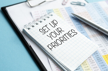 Obraz premium Business concept. On the business charts lies a pen, a notepad with note paper with the inscription - SET UP YOUR PRIORITIES
