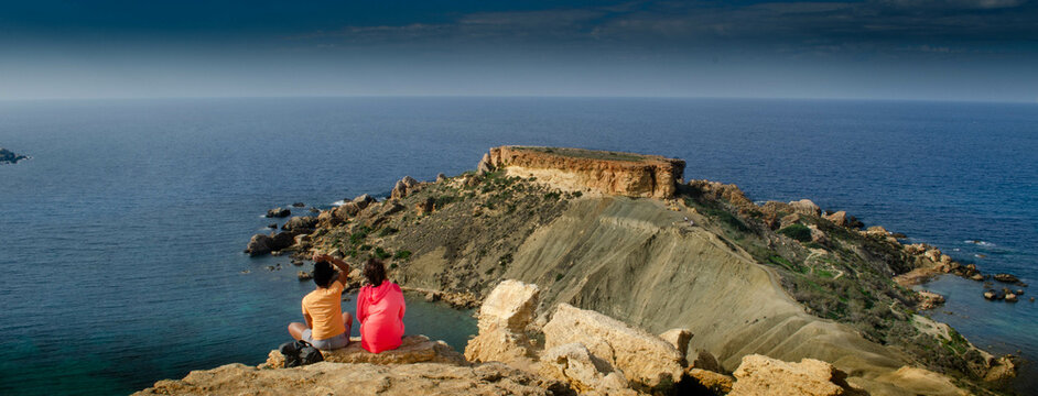  Two woman sitting on ege of Cliffside View Overlooking the Blue Sea