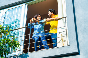 Indian couple in their thirties enjoying coffee and conversation on balcony in morning sun