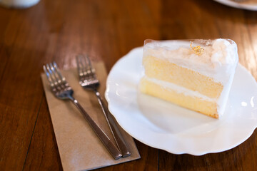 Coconut cake on a white plate on a wooden table in a bakery or coffee shop