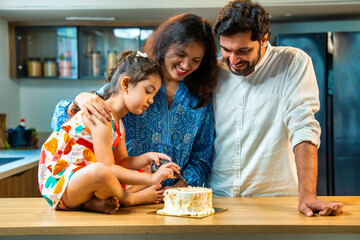 Indian asian Parents and little girl decorating a homemade cake together, writing her name