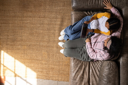 Grandma and asian female teenager bonding on couch, sharing tablet at home, copy space