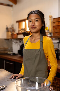 Asian female teenager in kitchen wearing apron, preparing for cooking at home