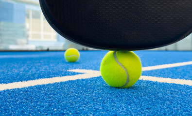 Black professional paddle tennis racket and ball with natural lighting on blue background....