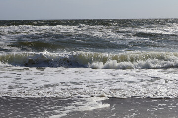 Dynamic waves crashing on the sandy shoreline under the bright daylight, showcasing the raw power of nature.