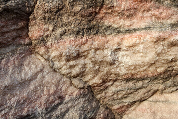 A detailed close-up of rugged natural stone texture featuring earthy brown and pinkish hues, ideal for backgrounds or geological studies.
