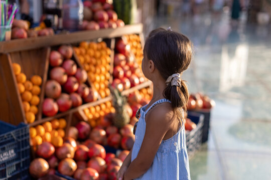 Child at a Market Stall with Pomegranates and Oranges  Awaits Fresh Juice
