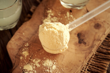 Whey protein powder in a measuring spoon with a glass of fresh whey