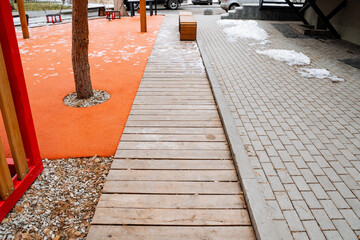 Obraz premium A wooden walkway gracefully directs visitors towards a playground that is located at the center, with a beautiful tree standing tall in the middle, creating a natural setting for play