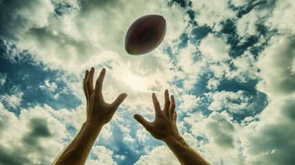 Hands catching football in mid-air, background of cloudy sky