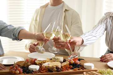 People clinking glasses of wine at served table, closeup