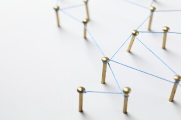 Obraz premium Network connection. Nails linked together by thread on white table, closeup. Space for text