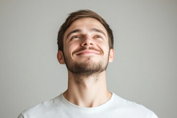 Obraz premium Young man with a sincere smile looking up with hope and positivity in a neutral setting