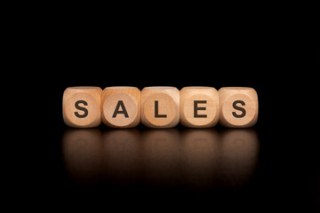 Wooden Dice Displaying the Word SALES on a Solid Black Background for Visual Impact