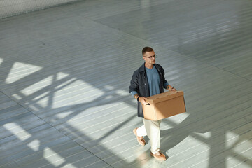 Full length shot of adult man carrying cardboard box with personal belongings walking towards self...