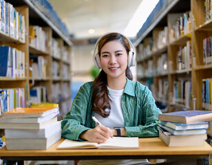 College student smiling and wearing headphones in library