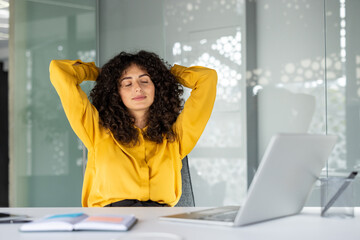 Young woman takes relaxing break at desk with laptop, enjoying moment of peace. Concept of workplace relaxation, mental health at work, and stress relief.