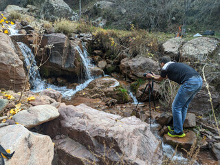 A photographer takes a photo or video of a beautiful autumn waterfall in the mountains. Vivid...