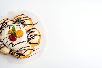 A plate of cream puff pastry drizzled with chocolate and topped with whipped cream, cherries, and mint, on a clean white background.