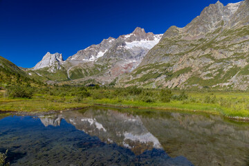 Naklejka premium Val Veny scenic landscape in Courmayeur valley, Italy on Tour du Mont Blanc hiking route. Alps beautiful landscape, scenic view of the alpine peaks, green fields and meadow with flowers and blue sky