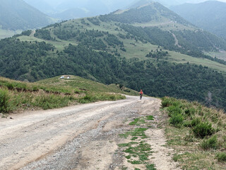 View of landcape with mountains and hills. A cyclist rides along the road. Dirt road on a hill....