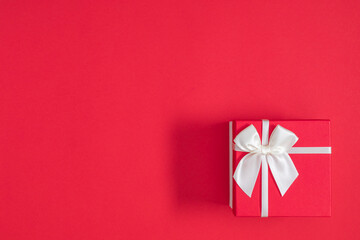 Red gift box with white bow on red background. Top view of red gift box. Flat lay. Copy space