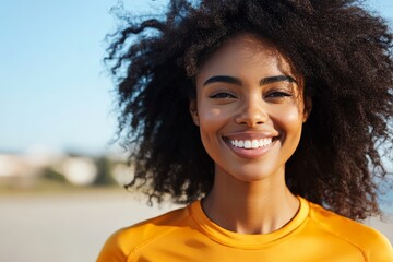 A cheerful woman with a vibrant afro is seen smiling broadly against a sunny backdrop, representing vitality, freedom, and joy in a carefree moment.