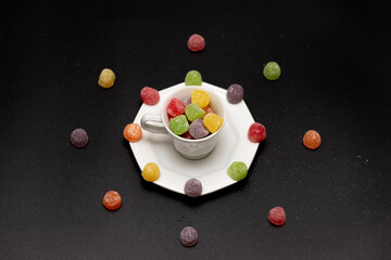 A coffee cup filled with flavorful, colorful gummy candies, also known as jujubes, surrounded by...