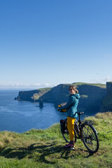 Woman on Cliff of Moher with bicycle loaded with bags, Digital nomad travels the world.