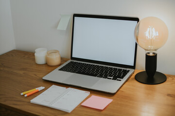 Working wooden table with laptop with white blank screen and calendar, table lamp, candles