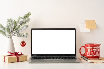 A still life cozy minimalist workspace with a laptop, festive decorations, and Scandinavian style. Features a red cup, gift box, and a small Christmas ornament creating a warm winter atmosphere