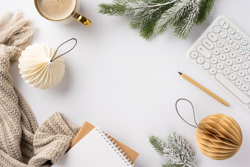 A cozy winter workspace setup featuring a keyboard, coffee, decorative ornaments, and green branches, evoking a warm and inviting atmosphere
