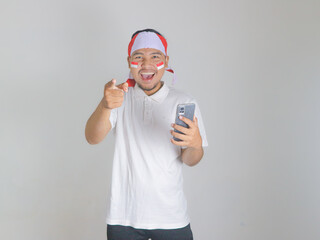 Excited young Asian men celebrate Indonesian independence day on 17 August while holding mobile phone and pointing forward isolated over white background