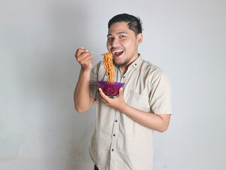 Handsome Asian man wearing a shirt is eating a bowl of spicy noodles