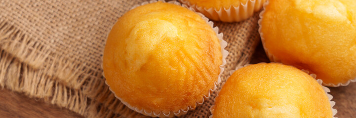 Four homemade muffins on a burlap surface. Soft golden color contrasts with the rustic background. Perfect for healthy snacks or comfort food moments. Close up