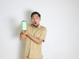 An Asian male Indonesian civil servant wearing a brown uniform stands while holding a cellphone...