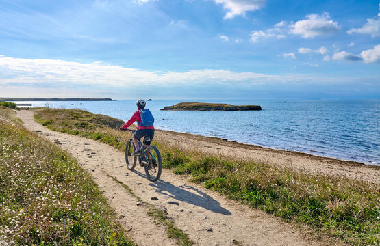 active senior woman cycling with her electric mountain bike at the wild coast of Quiberon peninsula, Brittany, France