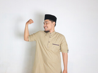 Excited young Asian Muslim man raising fists and celebrating victory on Ramadan isolated over white background. People religious Islam lifestyle concept